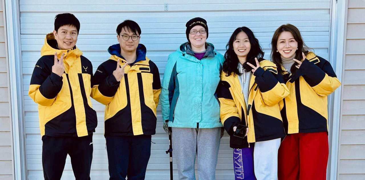 Five smiling people in colorful jackets pose together outdoors, making peace signs, embodying joyful independence.