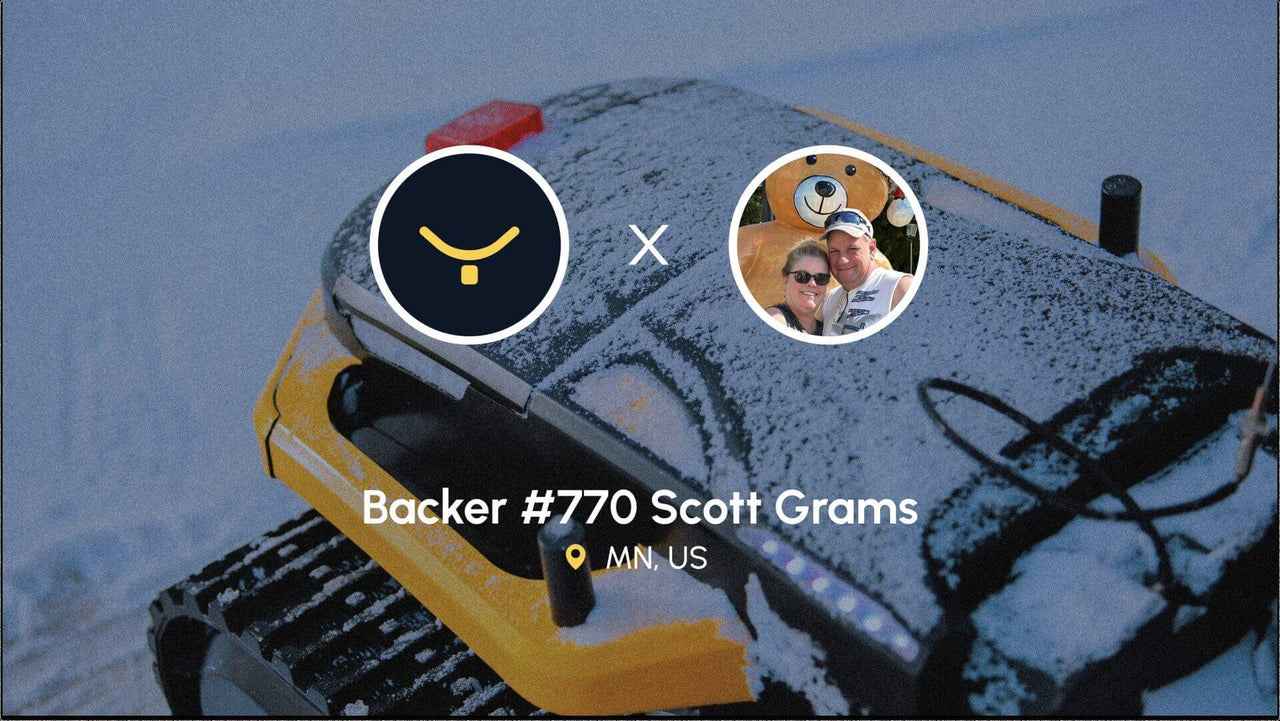 Snow-covered yellow snowmobile with Yarbo logo and photo of Scott Grams and partner smiling beside a giant bear statue.