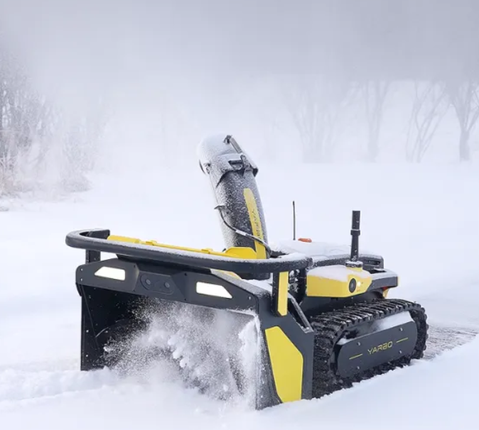 Yellow and black Yarbo snowblower clears deep snow with tracked movement, spraying snow in a wintry landscape.