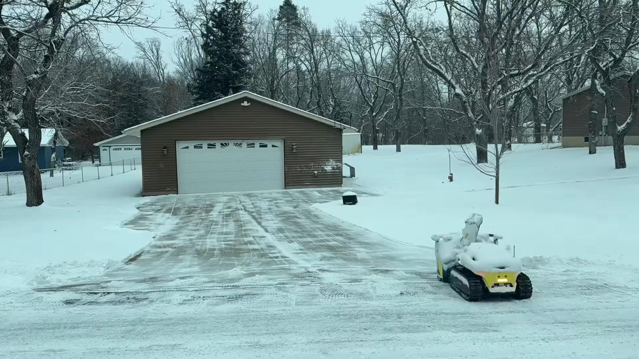 Electric snow blower clearing driveway in snowy suburban yard, garage in background, winter calm.