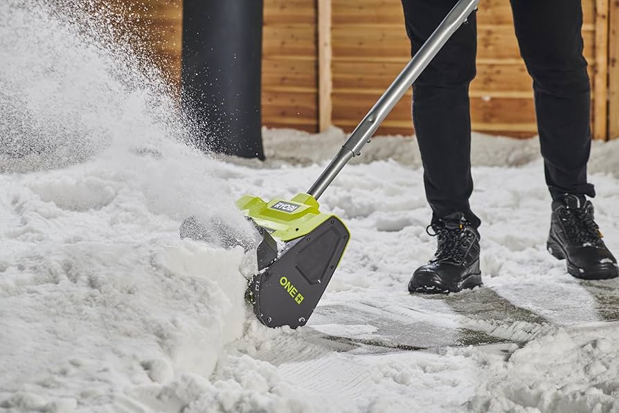 Person using green and black battery-powered snow shovel to clear snow from driveway, showcasing efficient winter maintenance.