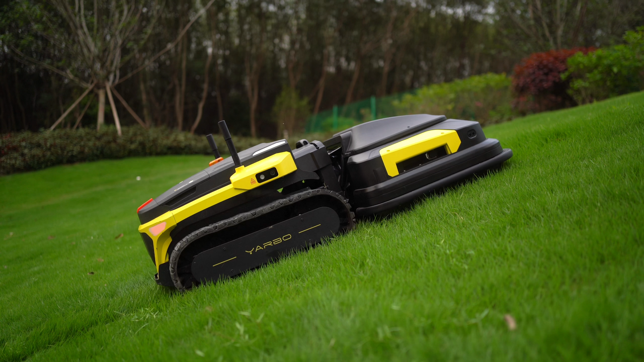 Yellow and black robot lawn mower with tank treads navigating a grassy slope in a lush garden.