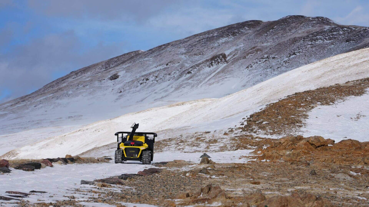 Yellow Yarbo robot navigates snowy mountain terrain, showcasing rugged innovation in remote exploration.