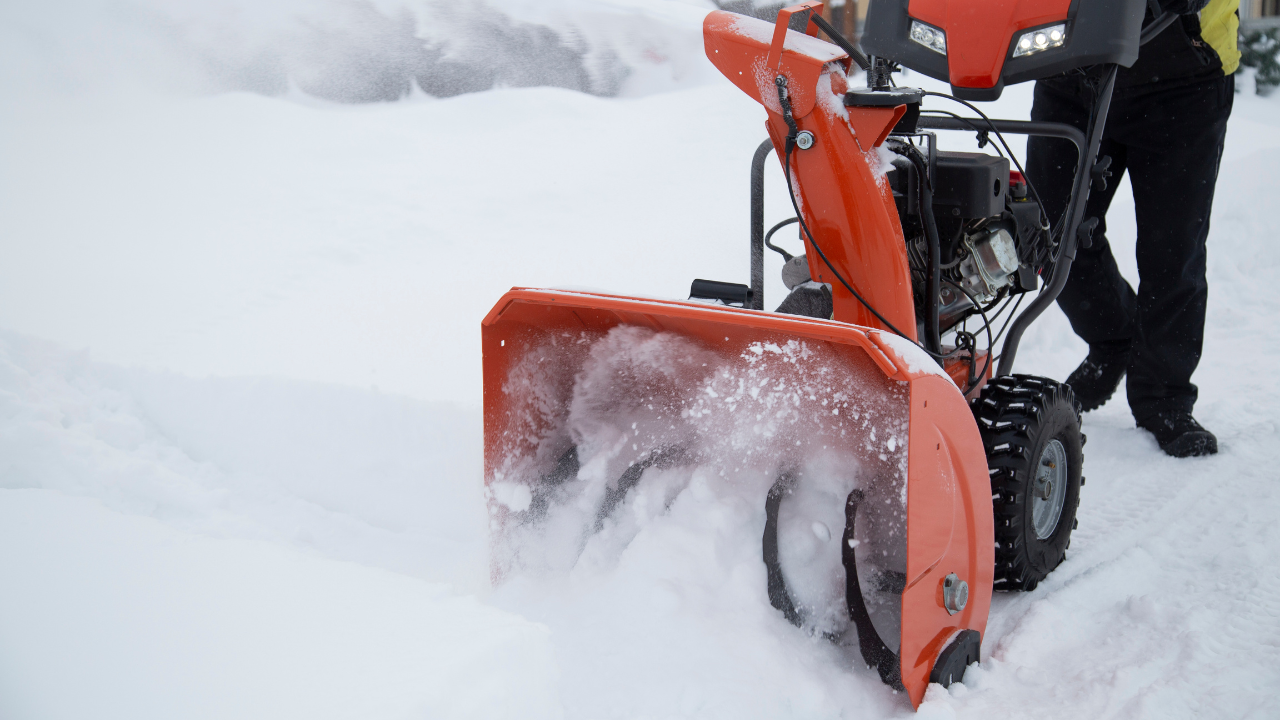 Bright orange snow blower clearing deep snow, operator in winter gear, cold outdoor scene.