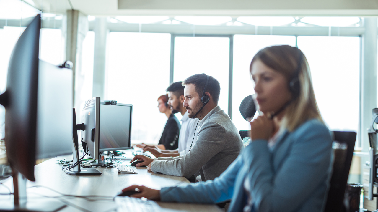 Support team at computers with headsets, assisting customers in bright, modern office.