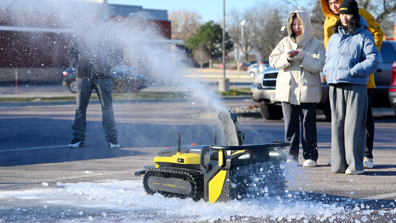 Yellow Yarbo robot clears ice on pavement as onlookers watch in winter gear during Madison event.