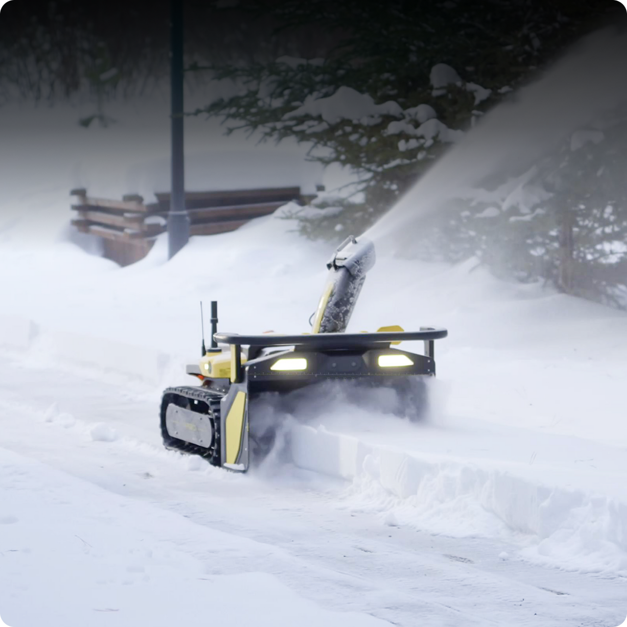 Yellow battery-powered snow blower clearing deep snow at night, bright lights cutting through winter storm.