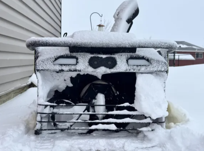 Snow-covered snowblower with frozen auger, stuck in snow, ready for winter repair.
