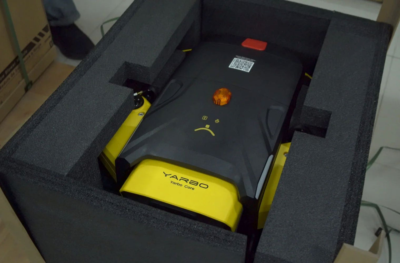 Yellow and black Yarbo Core robotic lawn mower nestled in protective foam packaging, ready for garage storage.