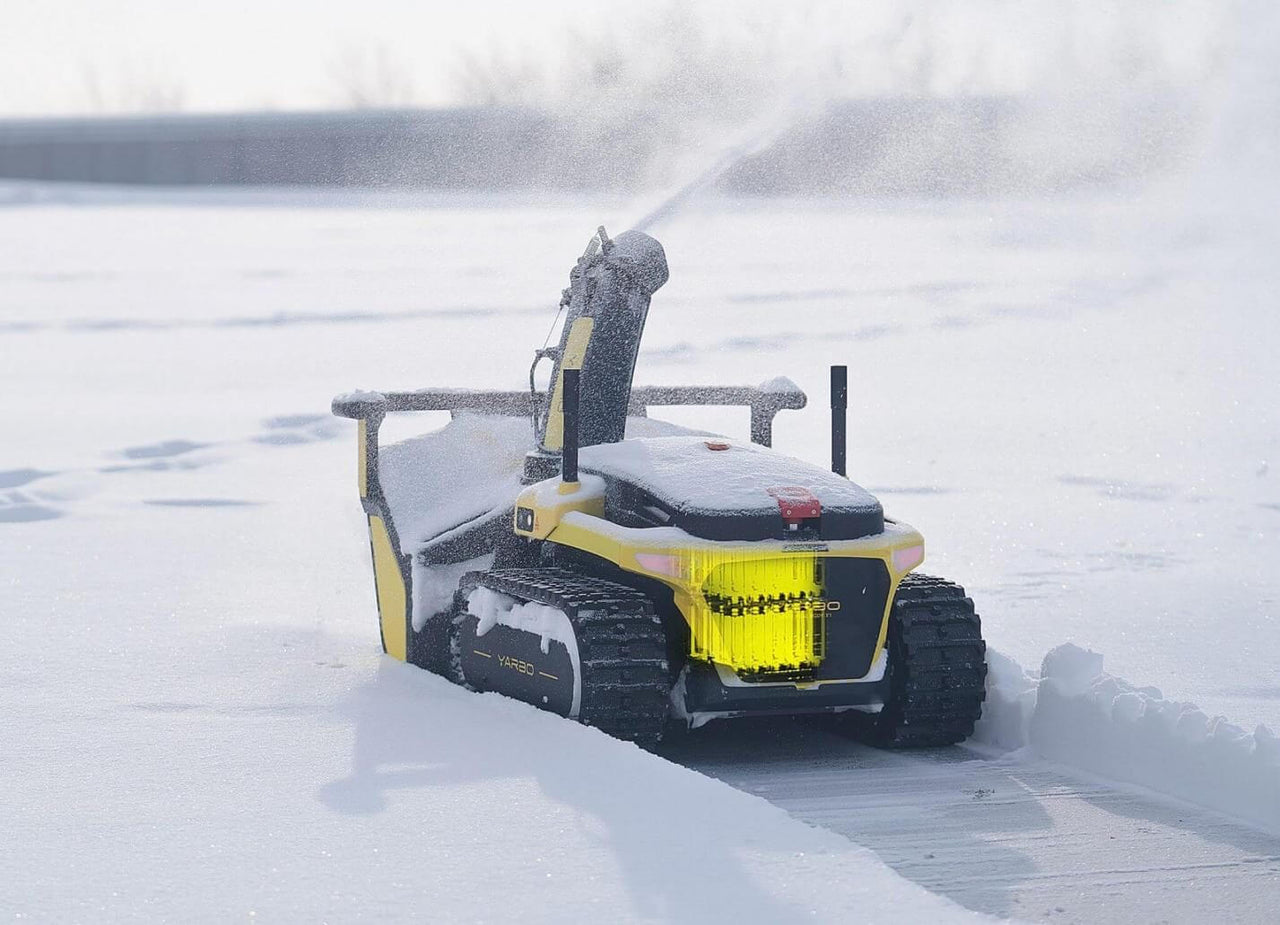 Yellow snow-clearing robot with tracks plows snow, showcasing durable design for heavy-duty winter maintenance.