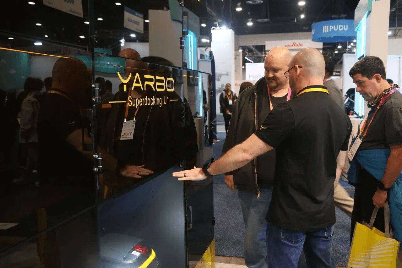 Two men examine Yarbo's Superdocking U1 at CES 2023, showcasing the robot's sleek design and interactive display.