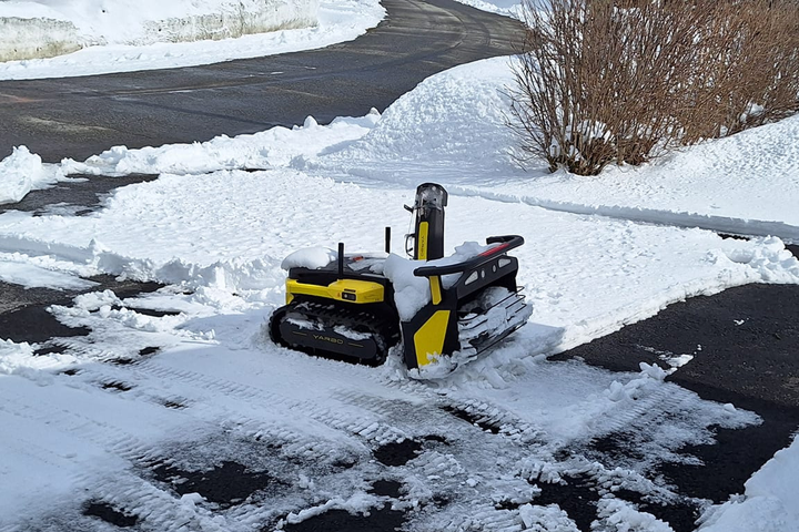 Yellow Yarbo snow robot navigates snowy, uneven driveway with tracked wheels, clearing path efficiently.