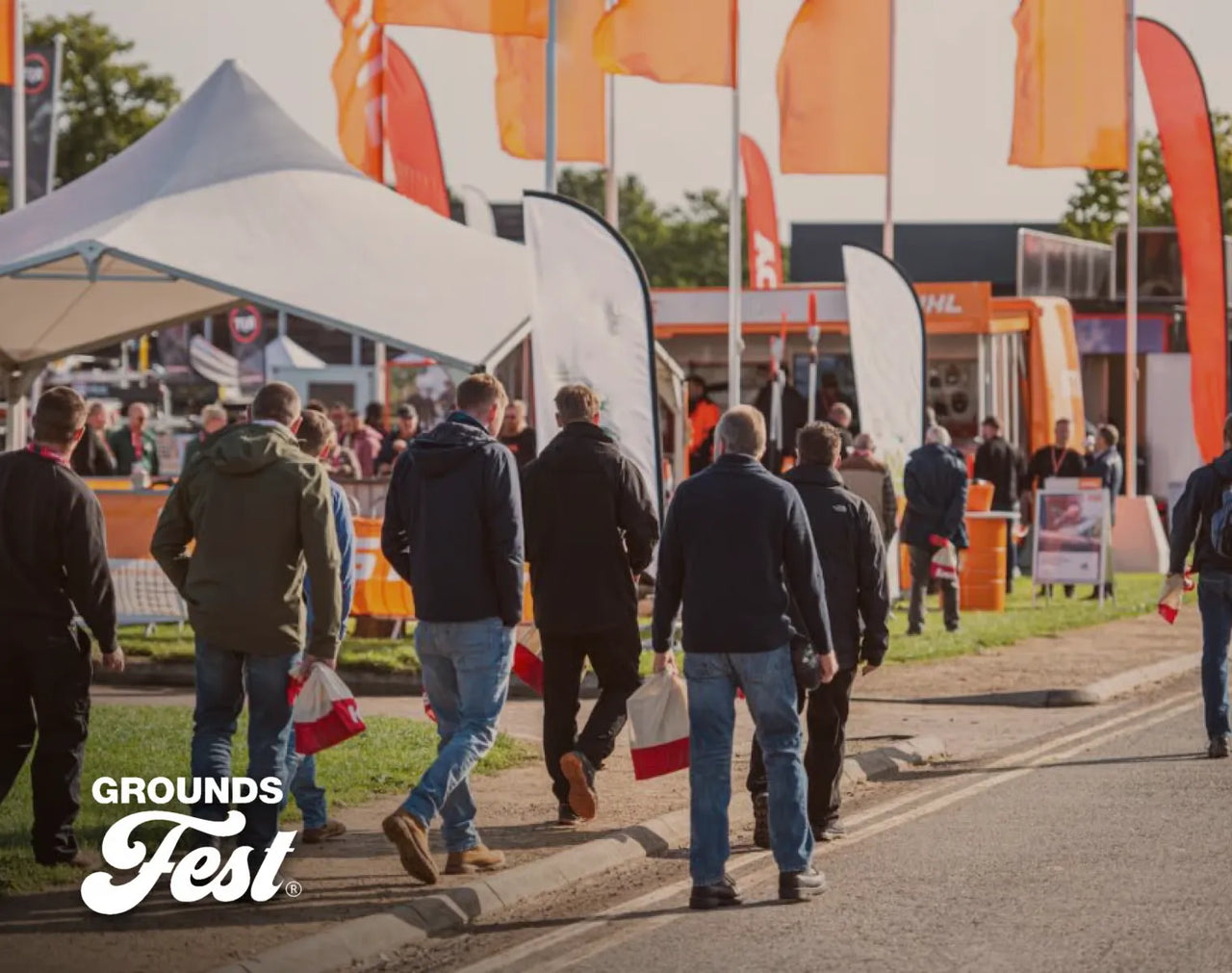 People walking toward vendor tents and orange flags at Grounds Fest outdoor event.
