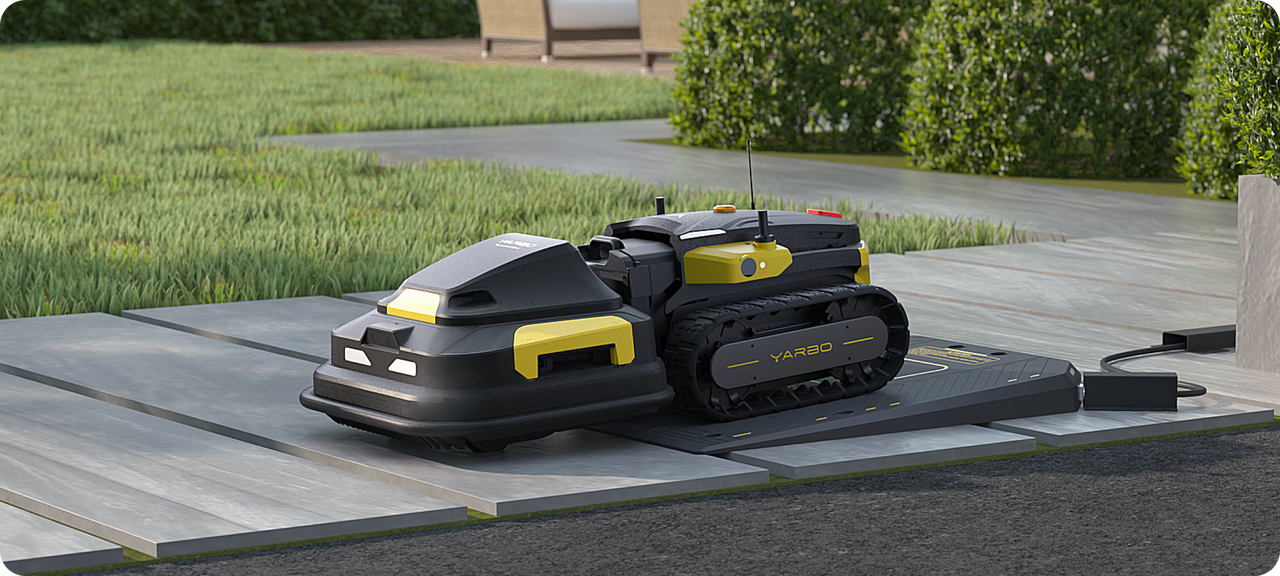 Black and yellow YARBO robotic lawn mower on charging dock in garden, with green grass and patio in background.