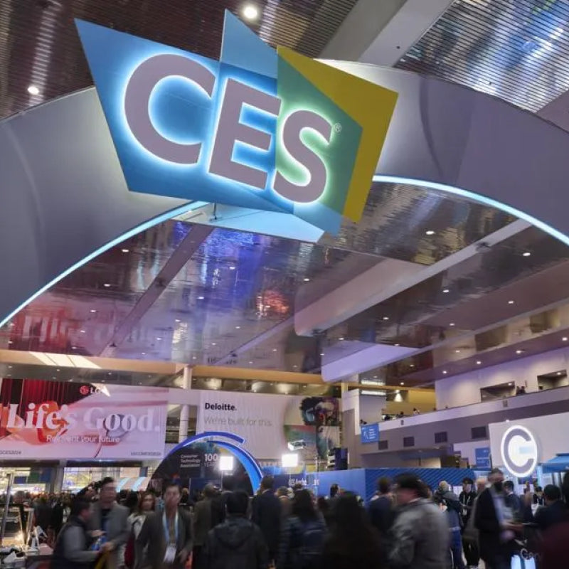 Bright CES logo in blue and yellow above a crowded convention hall with attendees and exhibitor booths below.