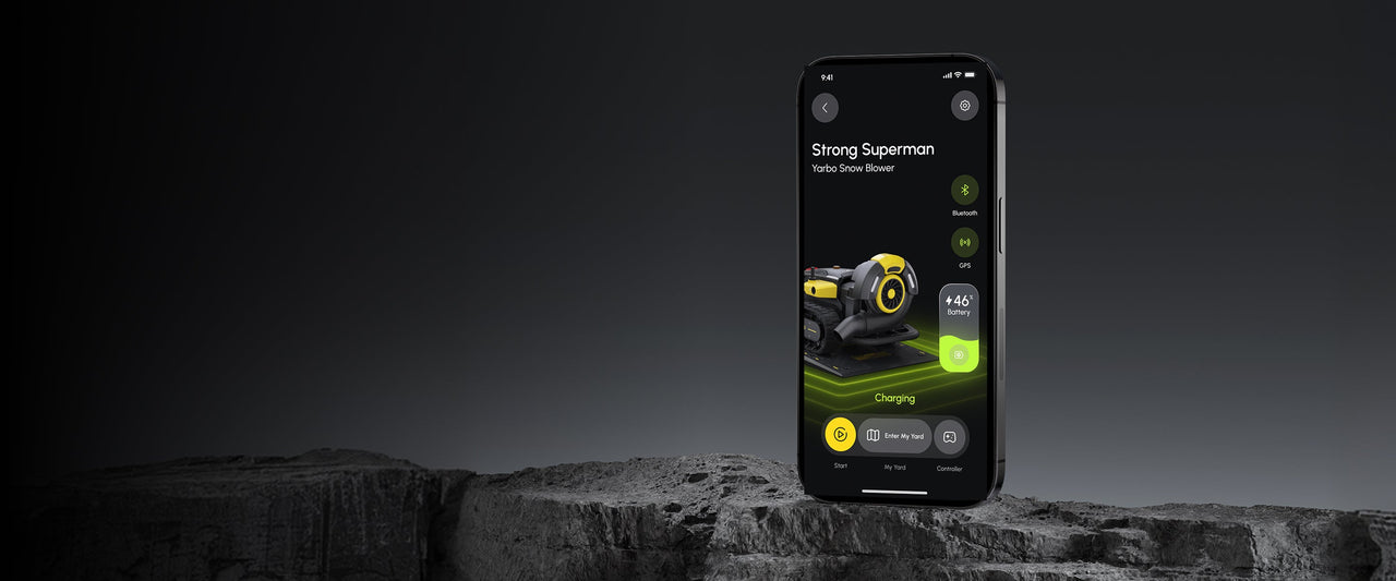 Smartphone displays app for "Strong Superman" Yarbo snow blower, showing 46% battery, charging, with Bluetooth and GPS icons, on dark rocky surface.