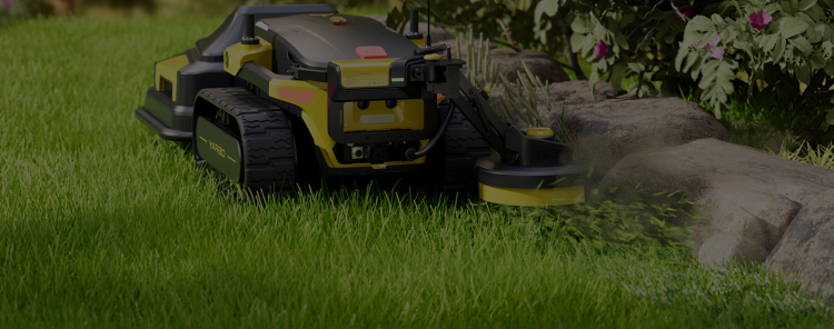 Yellow and black robotic lawn mower with tank treads cuts grass near rocks and flowers in a lush green yard.