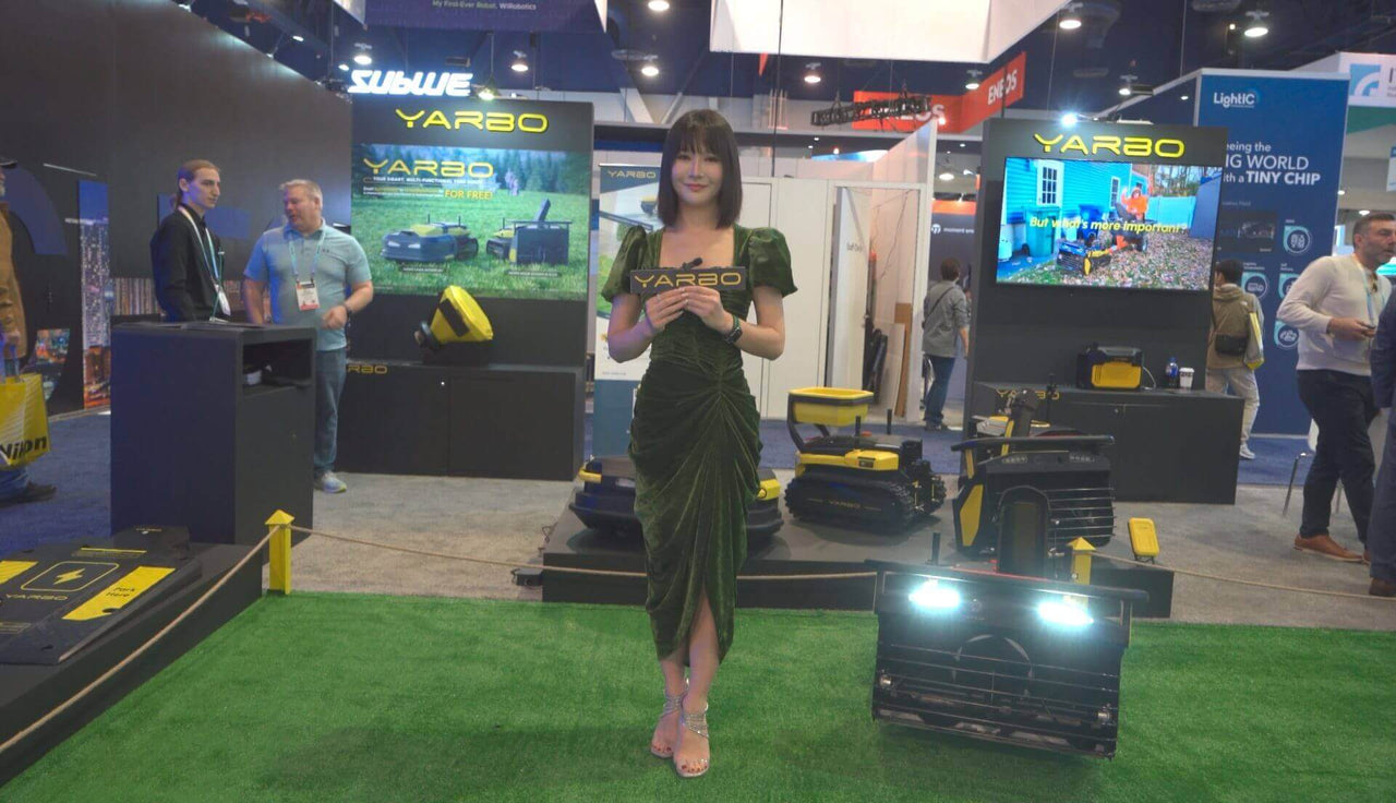 Woman in green dress holds YARBO sign at CES tech booth, surrounded by robotic lawn mowers and bright displays.