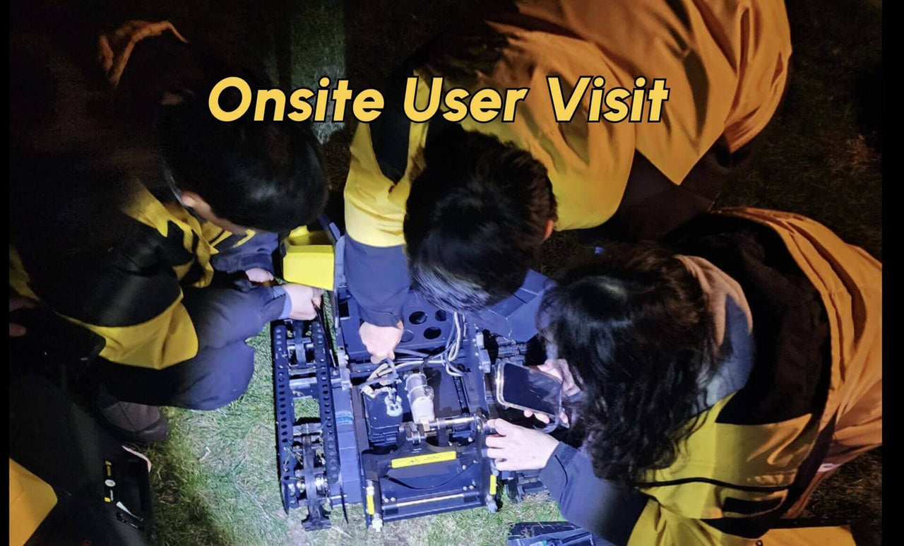 Three team members in yellow vests inspect a robotic machine on grass at night, collaborating closely during an onsite user visit.