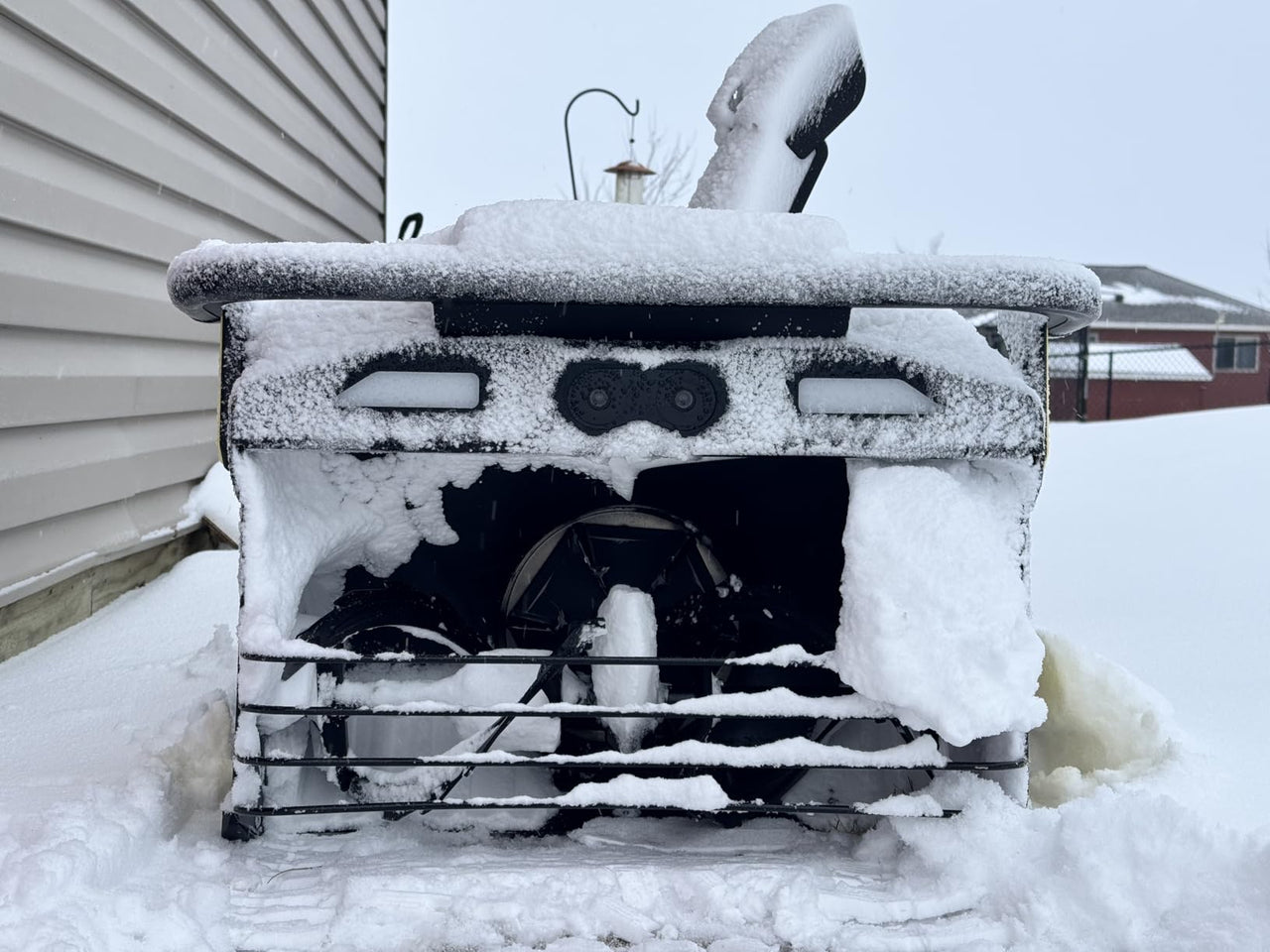 Snow-covered snow blower in winter yard, highlighting need for replacement parts and maintenance.