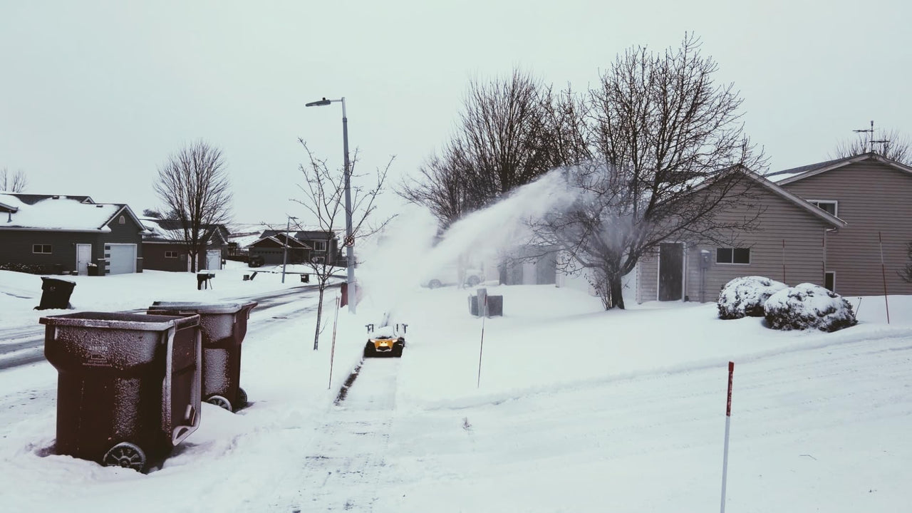 Snowblower clears driveway in snowy suburban neighborhood, showing winter prep in action.
