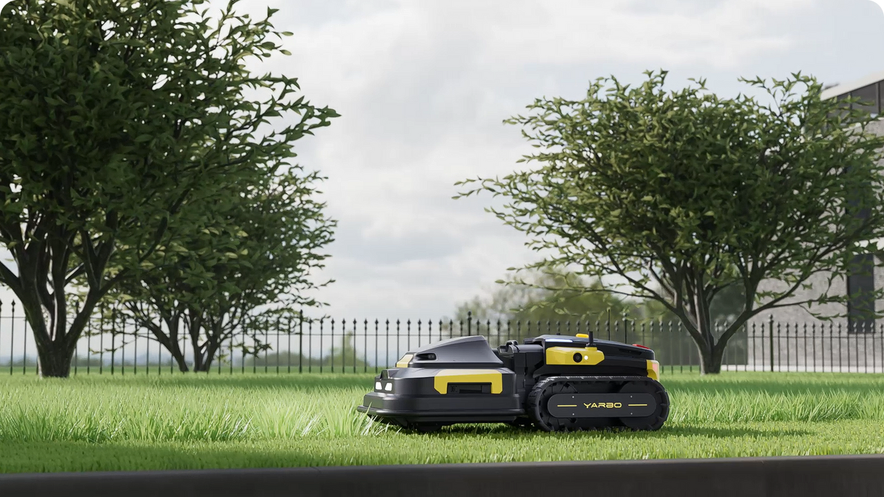 Black and yellow robotic lawn mower on lush green grass, framed by trees and a fence, showcasing efficient, hands-free mowing.