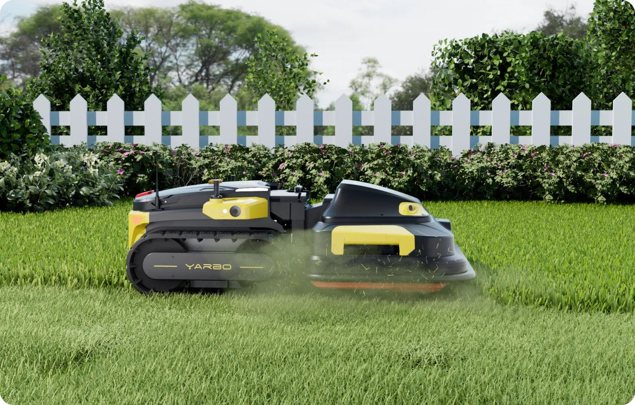 Yellow and black Yarbo robotic mower cuts lush green lawn, kicking up clippings near white picket fence and flowering shrubs.