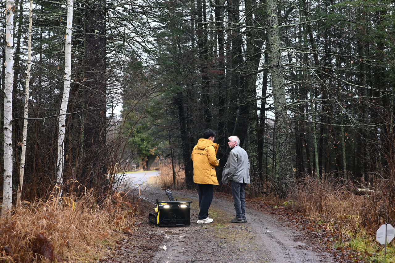 Two men converse on a forest path beside a glowing Yarbo portable power station, embodying innovation and community in nature.