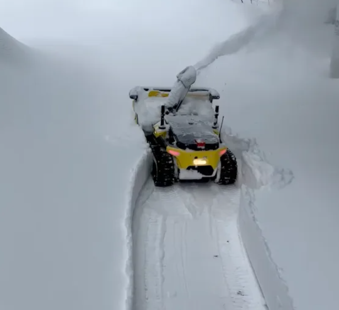 Yellow battery-powered snow blower clearing deep snow, creating a clean path in a snowy landscape.
