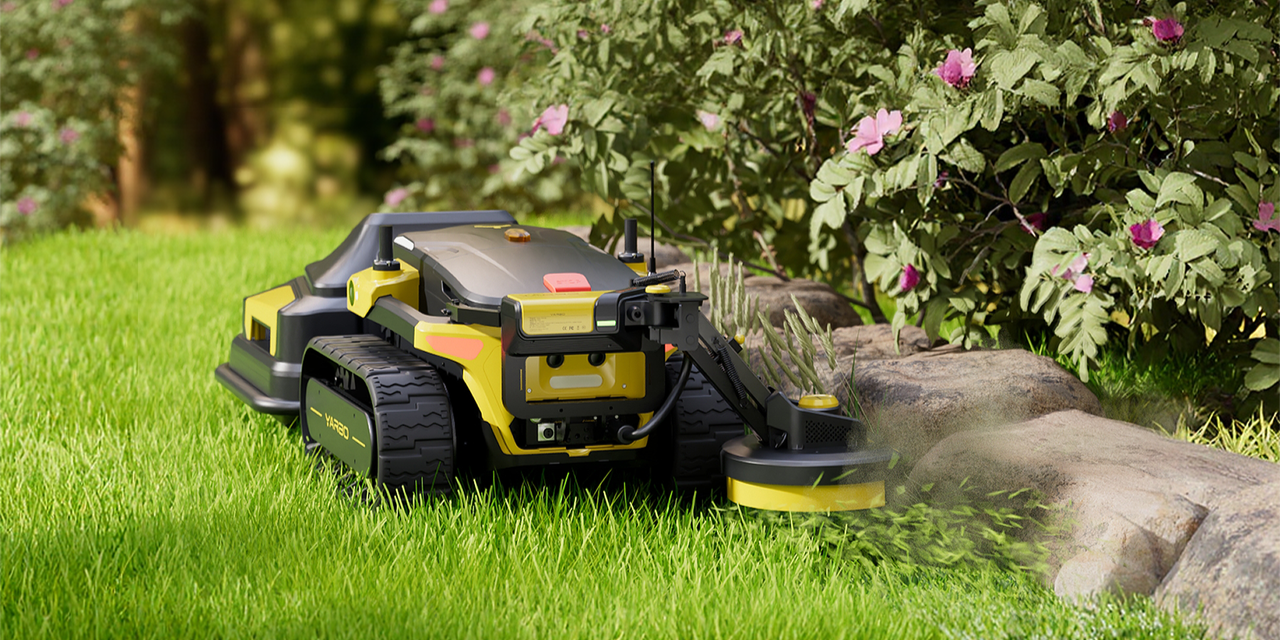 Yellow robotic lawn edger trims grass along rocks and pink flowers in a vibrant, well-kept garden.