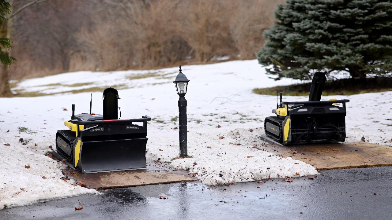 Two Yarbo snow blowers parked on wooden planks in snowy yard, ready for winter storage.