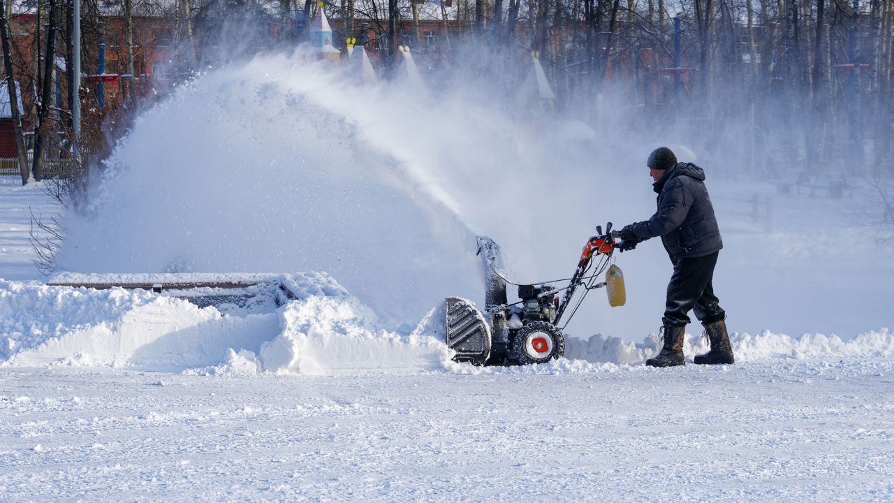 Man operates gas-powered snow blower, clearing deep snow in bright winter yard.