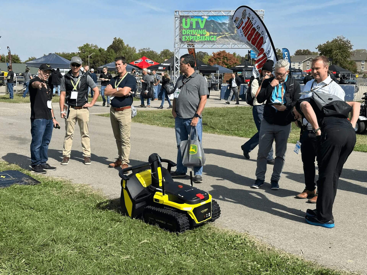 Yellow and black Yarbo yard robot on grass at Equip Exposition 2023, drawing crowd attention at outdoor trade show.