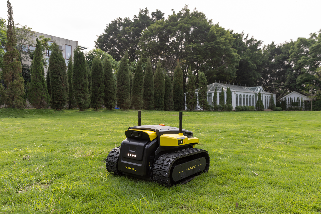 Yellow and black Yarbo Core robot mowing lush green lawn, sleek design with tank treads, modern garden setting.