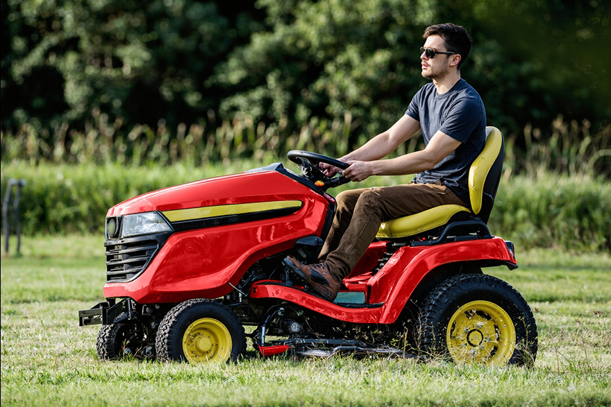 Man driving red riding lawn mower on sunny grassy yard, relaxed and focused, yellow accents gleaming.