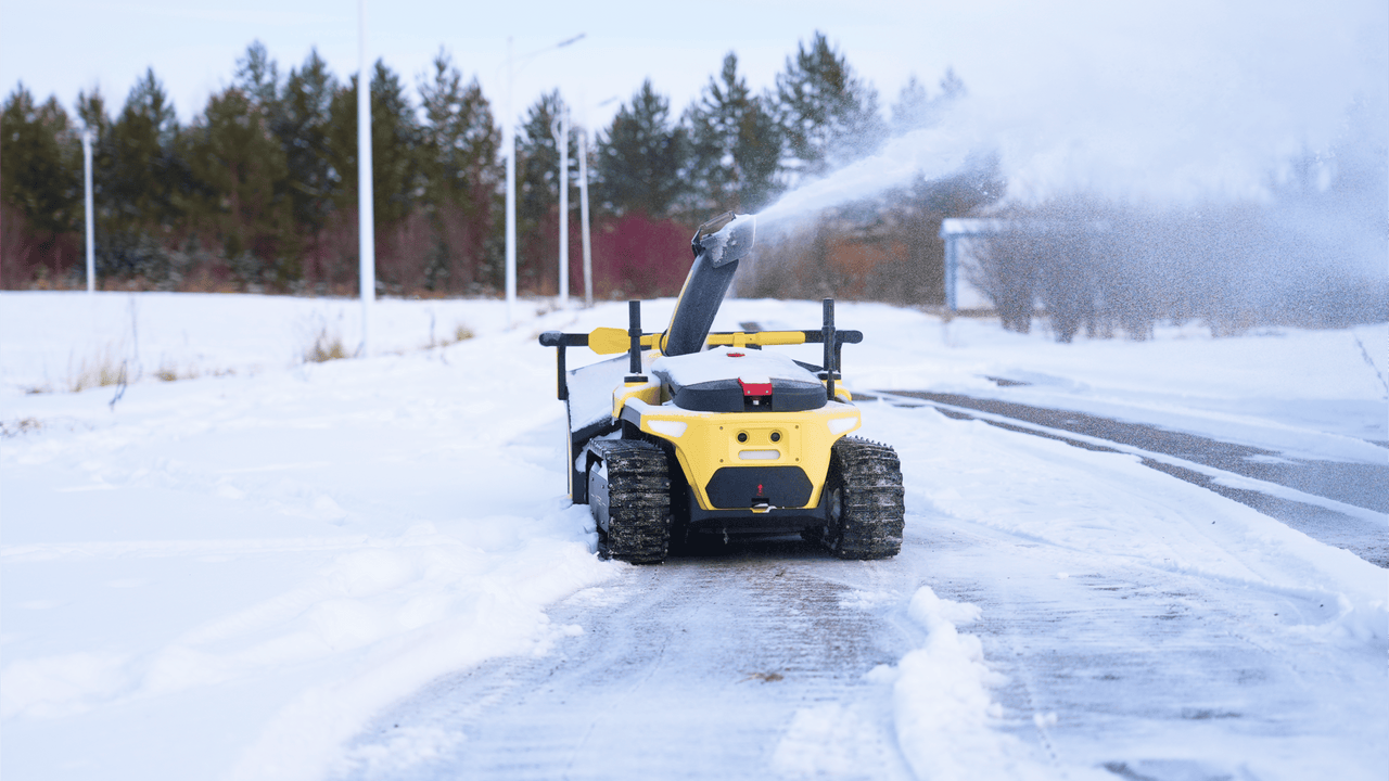 Yellow snow blower clearing a snowy driveway, powerful spray clearing path, winter maintenance in action.