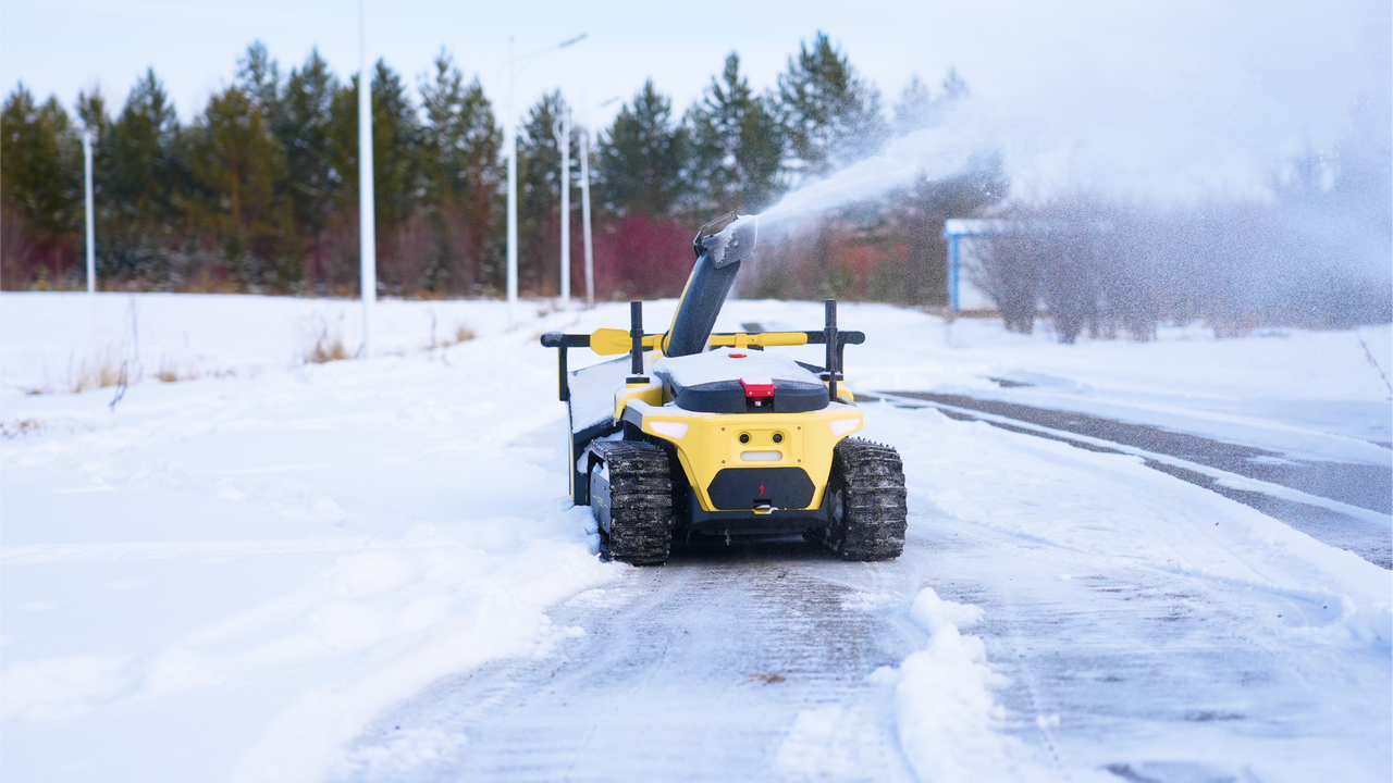 Yellow snow blower clearing sidewalk, spraying snow into air on winter day, efficient winter cleanup in action.