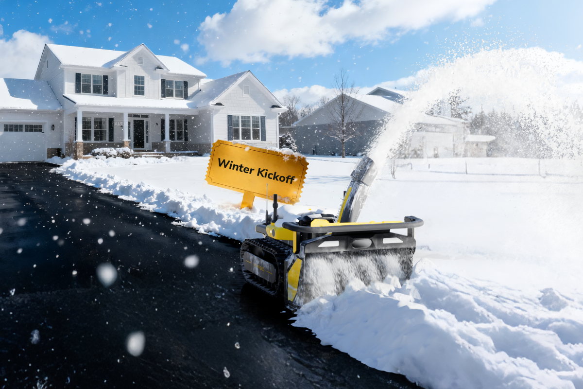 Yellow snow blower clearing driveway in front of snowy home, with "Winter Kickoff" sign, bright blue sky, and falling snow.