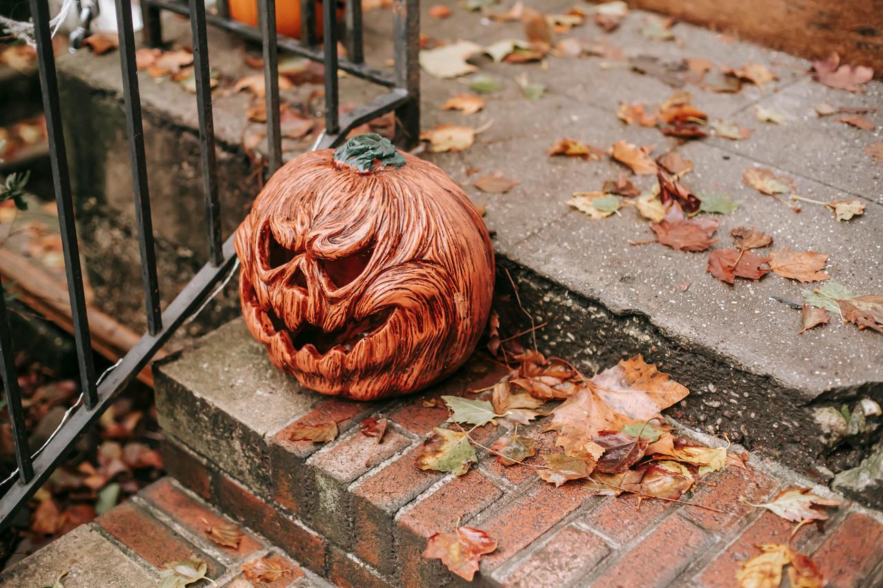 Scary carved pumpkin sits on brick steps with fallen leaves, evoking autumn chill and winter prep.
