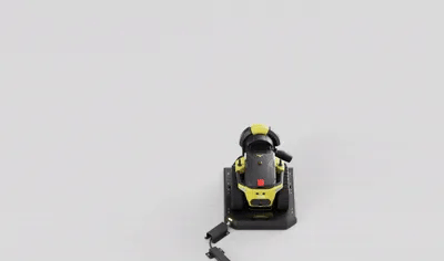 Black and yellow power sander with red button, viewed from above on a light gray background.