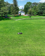 Black and yellow robotic lawn mower by Yarbo on lush green grass in a spacious backyard, side view, lifestyle setting