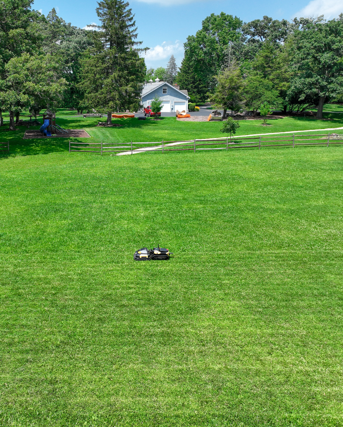 Black and yellow robotic lawn mower by Yarbo on lush green grass in a spacious backyard, side view, lifestyle setting