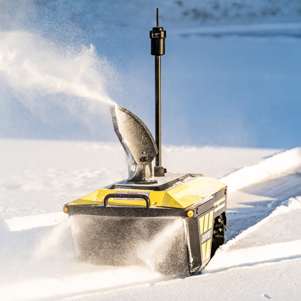 Yellow snow blower ejecting snow on snowy ground, bright sunlight, black chute and handle, snow-covered background.