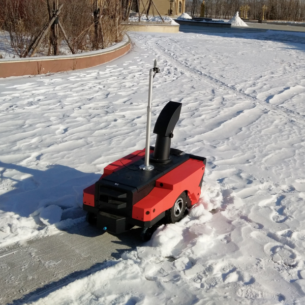 Red and black robotic snow blower clearing snow on a sunny day, leaving a cleared path behind.