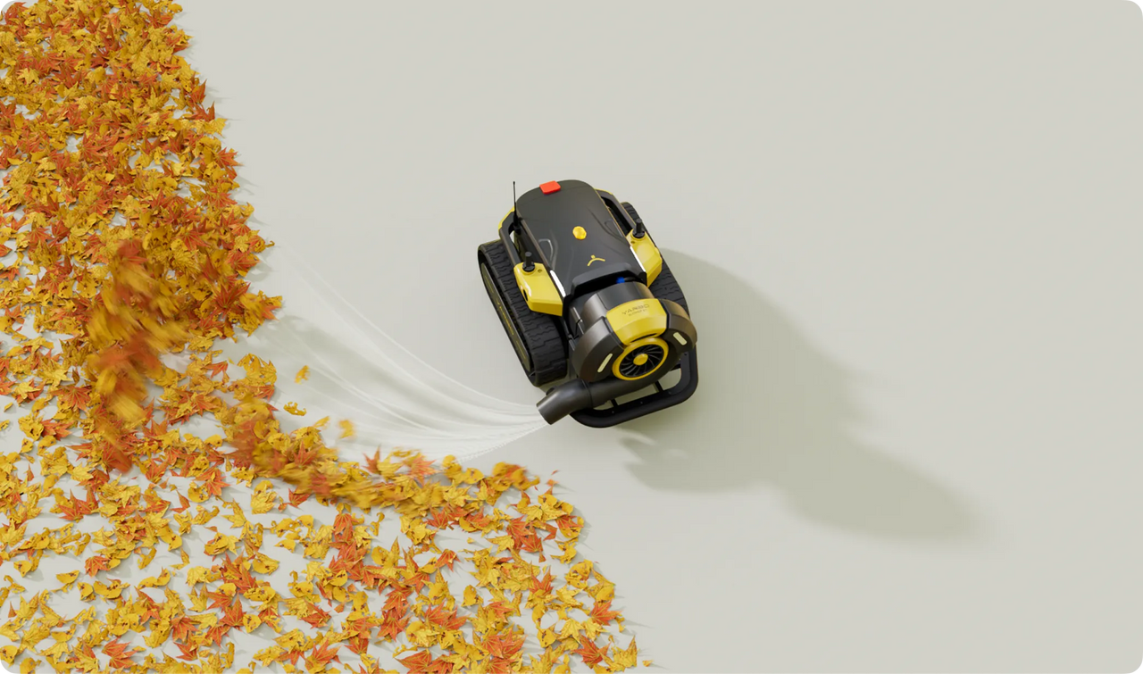 Black and yellow robotic leaf blower clearing orange and yellow autumn leaves on a light gray surface.