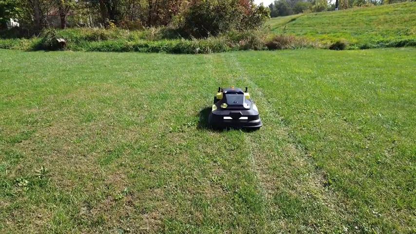 Black and yellow robotic lawn mower on green grass, trees in background, sunny day.