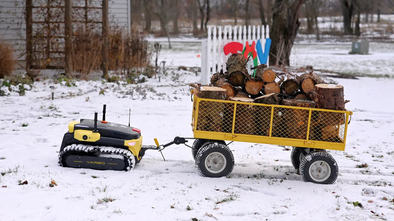 Yellow and black YARBO robot tractor pulls a yellow wagon full of logs across snowy yard.