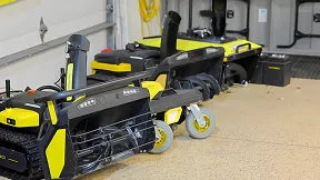 Yellow and black Ryobi power tools on wheeled carts in a garage, with tools and storage boxes in background.