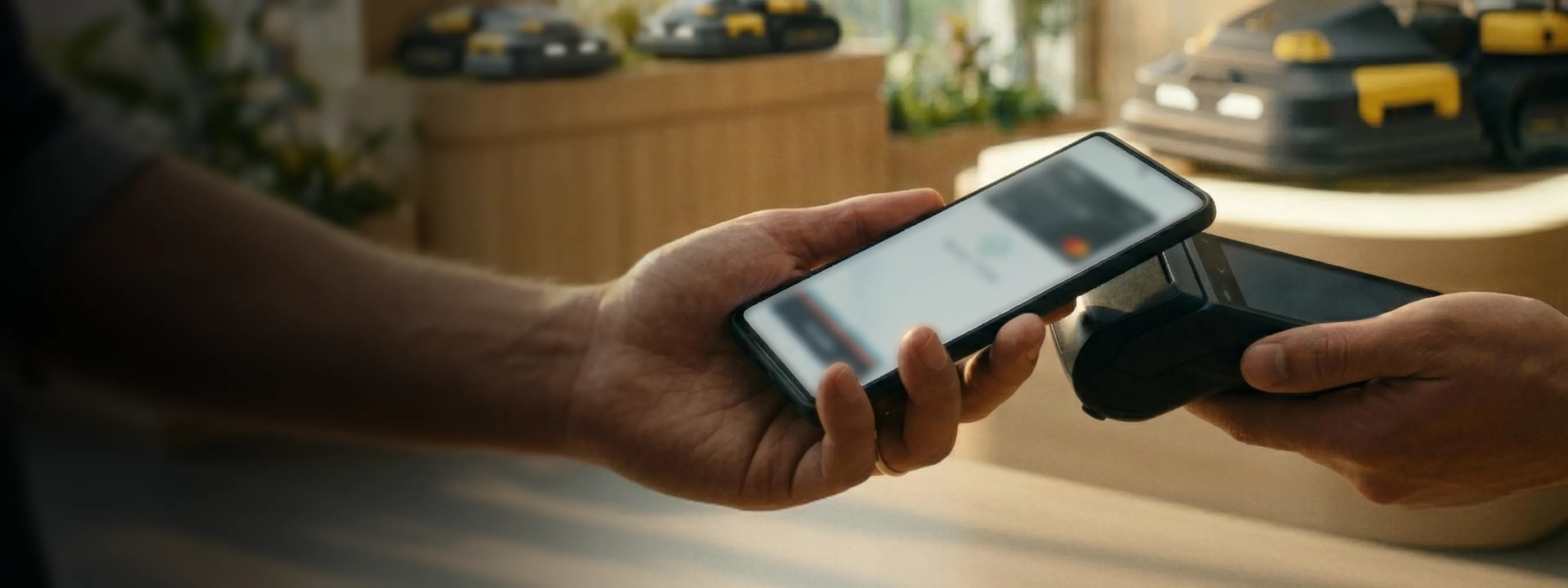 Hands holding smartphone and payment terminal, making contactless payment in bright, modern store.