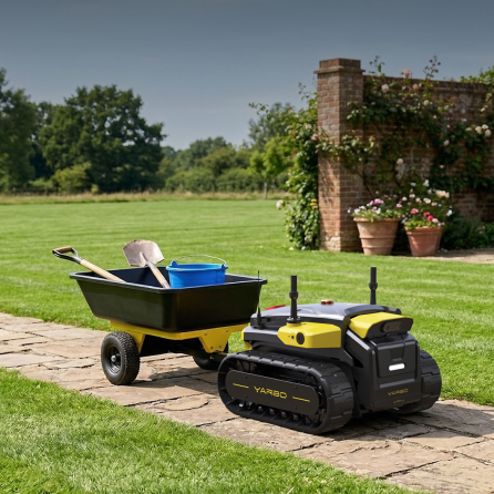 Yellow and black YARBO robotic lawn mower on stone path beside wheelbarrow with tools, green lawn and brick wall in background.